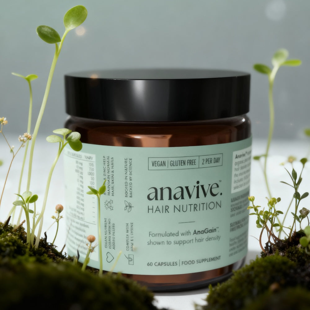 Anavive hair nutrition supplement jar surrounded by small pea shoots sprouting out of moss on a light background