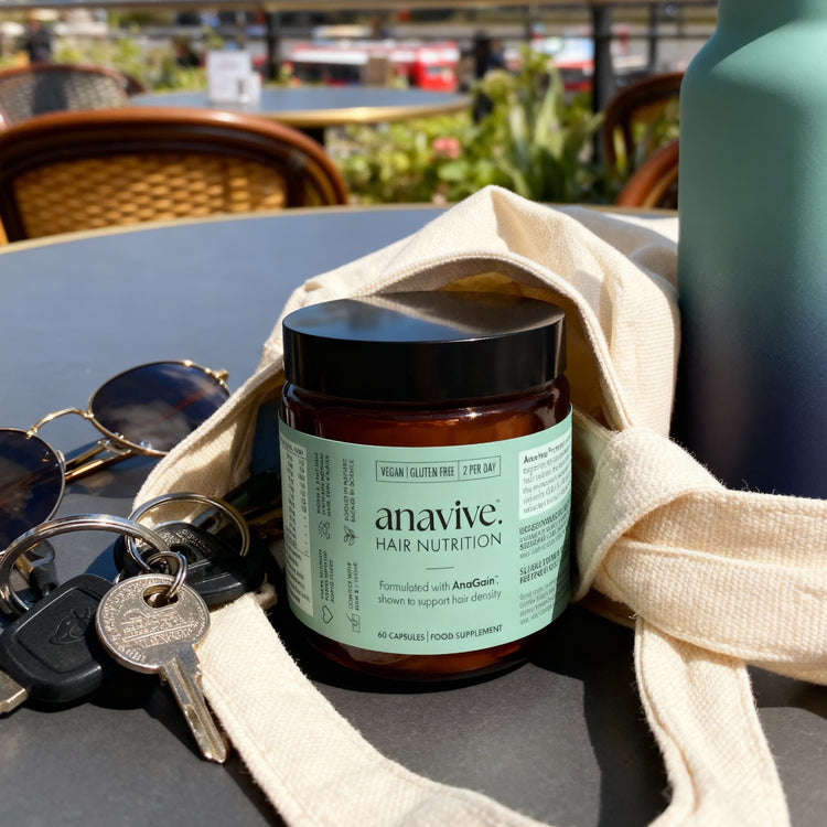 Mockup of Anavive hair nutrition bottle sat on an outdoor table under a tote bag and next to car keys