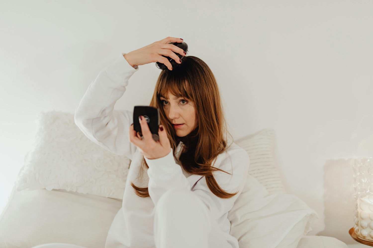 Woman sitting on a couch using a hair dryer and phone.